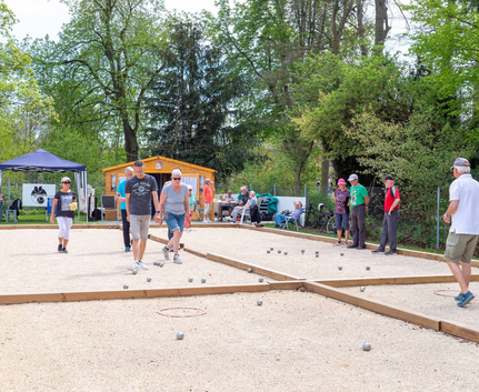 Gruppe Menschen spielt Petanque auf Sandbahnen mit Metallkugeln unter Bäumen
