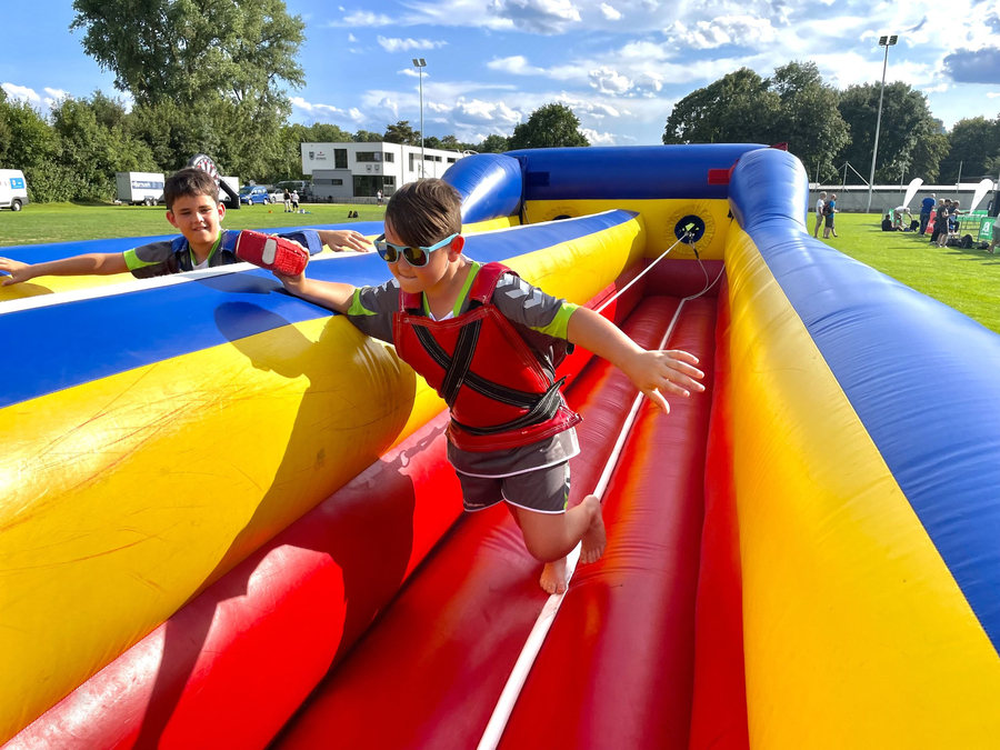 Schwörsporttag SSV Ulm 1846 e.V. Zwei Jungen balancieren auf buntem aufblasbaren Hindernis einer mit Sonnenbrille