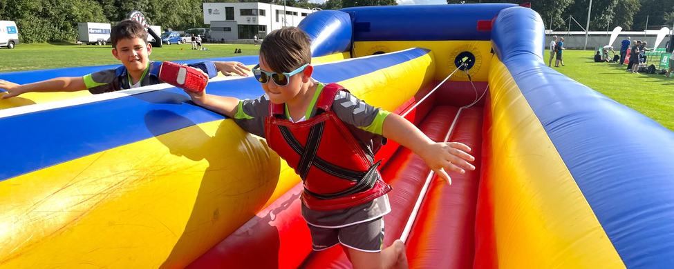 Schwörsporttag SSV Ulm 1846 e.V. Zwei Jungen balancieren auf buntem aufblasbaren Hindernis einer mit Sonnenbrille