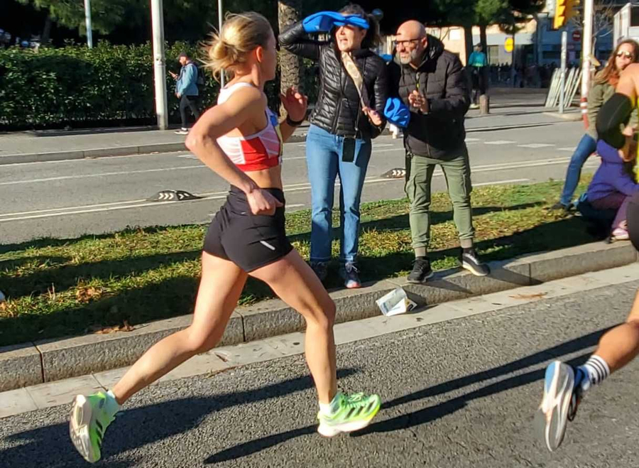 Läuferin im roten Trikot und grünen Schuhen läuft vorbei an jubelnden Zuschauern