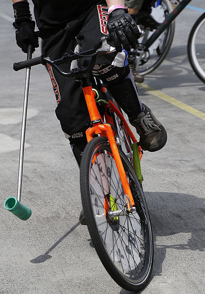 Cyclist on orange bicycle holding green mallet wearing knee pads