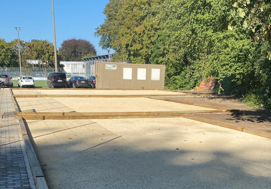 Gravel playing courts with wooden borders next to paved walkway
