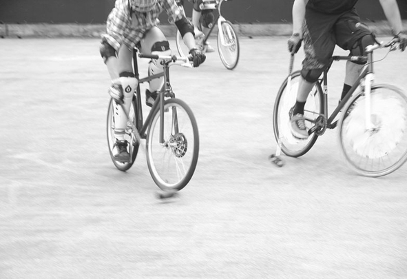 Three cyclists wearing knee pads riding on paved court
