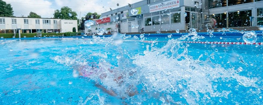 Spritzendes Wasser über Schwimmer im Freibad vor Vereinsgebäude