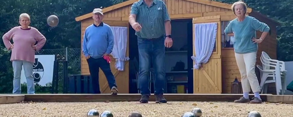 Vier Teilnehmende spielen Boule auf Kiesbahn vor Holzschuppen