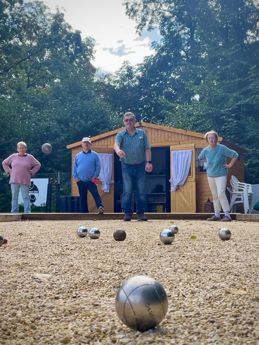 Vier Teilnehmende spielen Boule auf Kiesbahn vor Holzschuppen