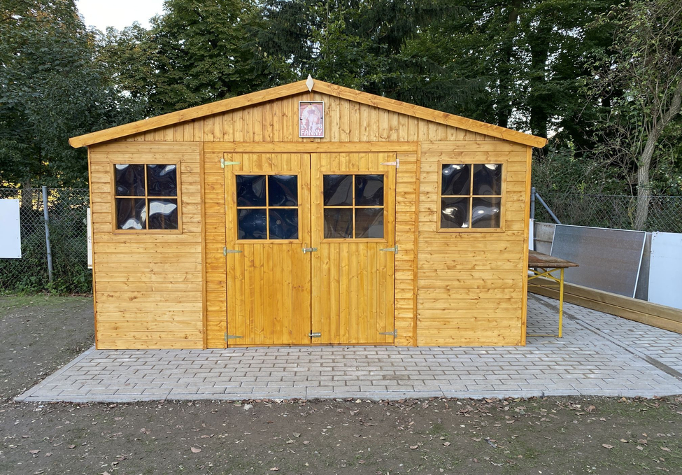 Holzschuppen mit Doppeltür und Seitenfenstern auf gepflastertem Untergrund