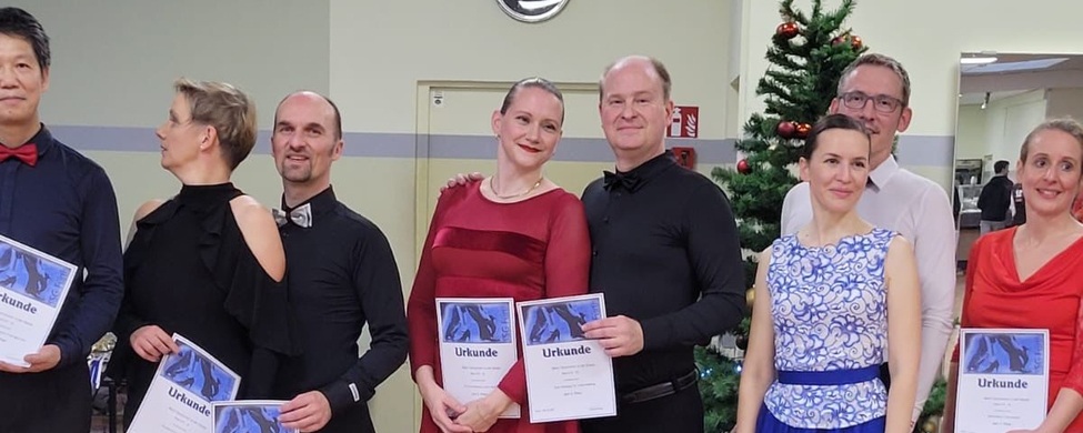 Mehrere Tanzpaare in Abendkleidung halten Urkunden vor Weihnachtsbaum