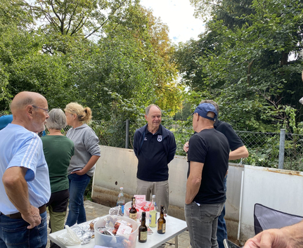 Mehrere Erwachsene stehen draußen an Tisch mit Getränken und Snacks
