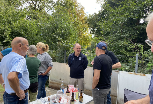 Mehrere Erwachsene stehen draußen an Tisch mit Getränken und Snacks