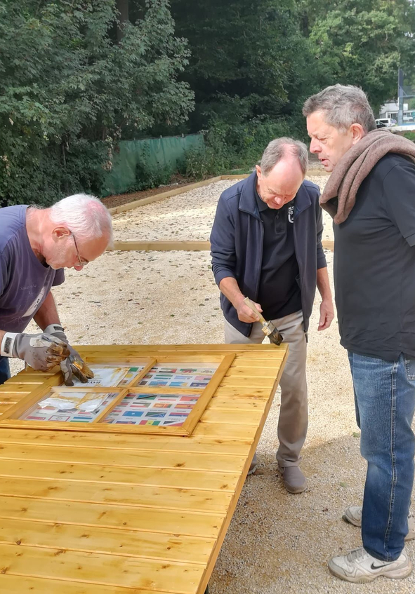 Three men staining a wooden tabletop outdoors