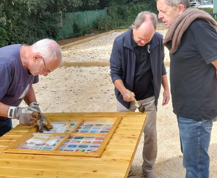 Three men staining a wooden tabletop outdoors