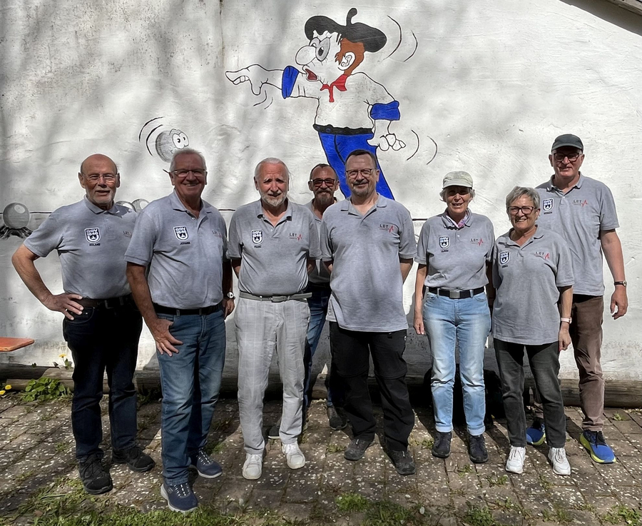 Acht Personen in grauen Poloshirts vor Wandgemälde mit Cartoonfigur