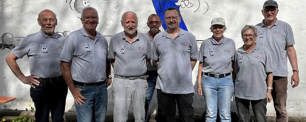 Acht Personen in grauen Poloshirts vor Wandgemälde mit Cartoonfigur