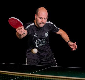 Sportlehrer beim Tischtennis schlägt weißen Ball mit rotem Schläger
