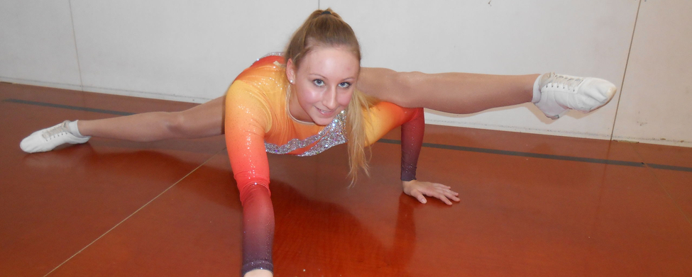 Athletin in orangefarbenem Trikot macht weite Bodenspreizung