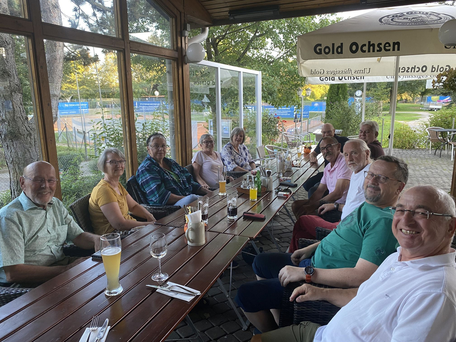 Gruppe Erwachsener an langem Holztisch unter Sonnenschirm mit Aufschrift Gold Ochsen