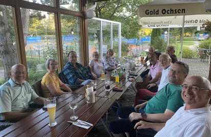 Gruppe Erwachsener an langem Holztisch unter Sonnenschirm mit Aufschrift Gold Ochsen