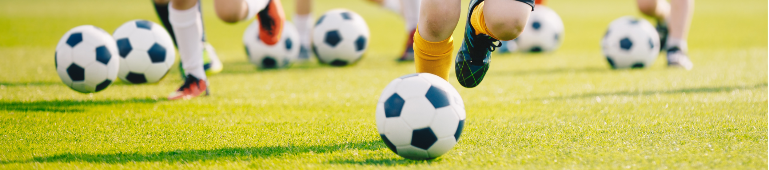 Kinder dribbeln Fußballbälle auf Rasen im Training der Fußballschule