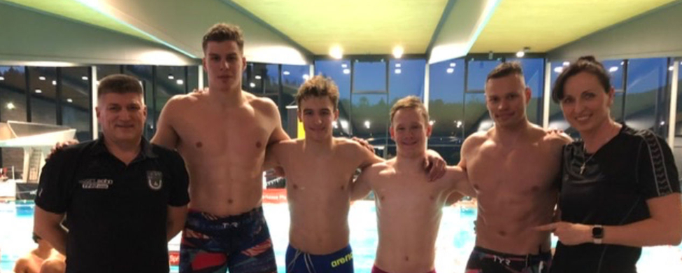 Vier jugendliche Schwimmer mit zwei Trainern vor Hallenbadbecken