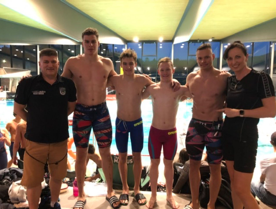 Vier jugendliche Schwimmer mit zwei Trainern vor Hallenbadbecken