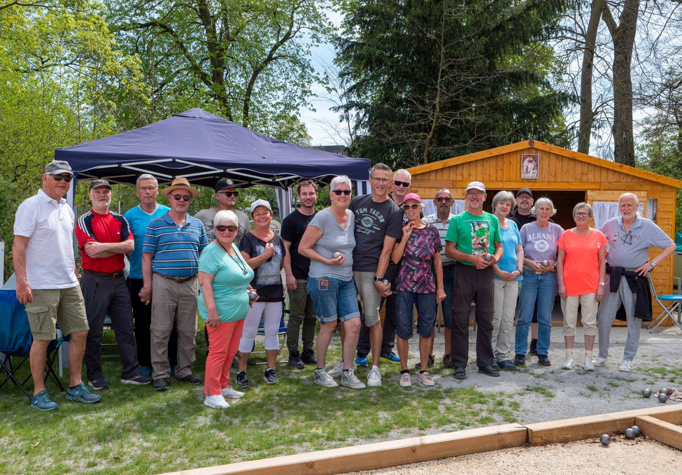 Gruppe von Erwachsenen mit Boulekugeln auf Bouleplatz vor Holzhütte