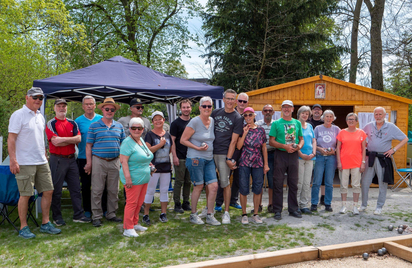 Gruppe von Erwachsenen mit Boulekugeln auf Bouleplatz vor Holzhütte