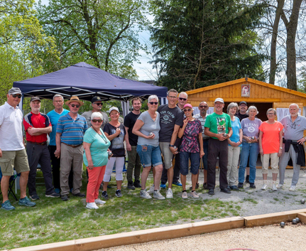 Gruppe von Erwachsenen mit Boulekugeln auf Bouleplatz vor Holzhütte