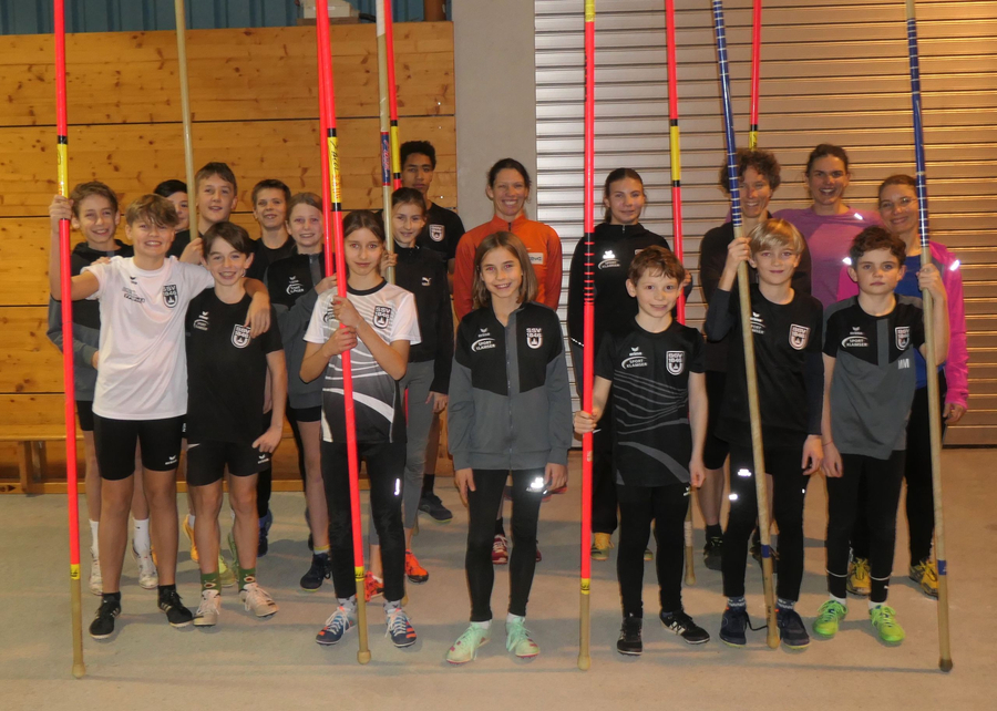 Gruppe von Nachwuchsathleten mit Stabhochsprungstangen in Sporthalle