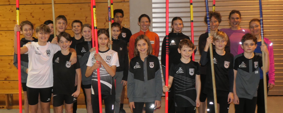Gruppe von Nachwuchsathleten mit Stabhochsprungstangen in Sporthalle