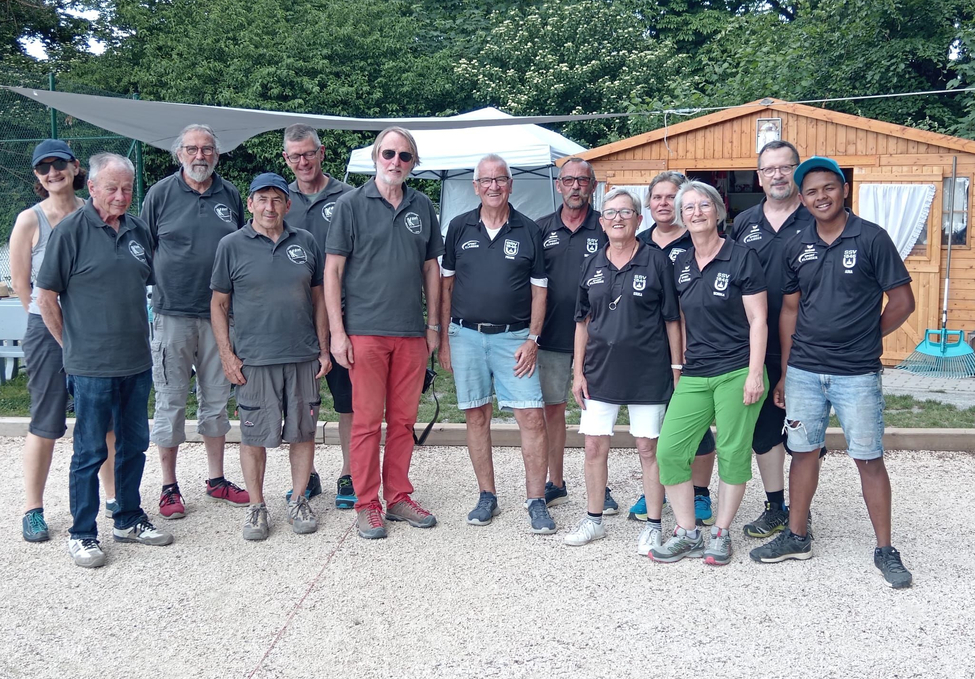 Gruppe von Personen in dunklen Poloshirts vor Holzhaus