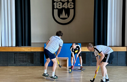 Drei Spieler spielen Hockey auf Rollbrettern vor SSV 1846 Emblem