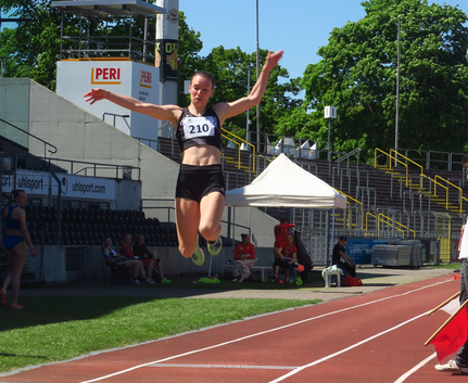 Athletin mit Startnummer 210 in der Luft beim Weitsprung