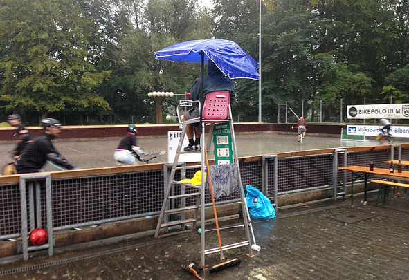 Schiedsrichter auf Leiter unter blauem Regenschirm beim Bikepolo