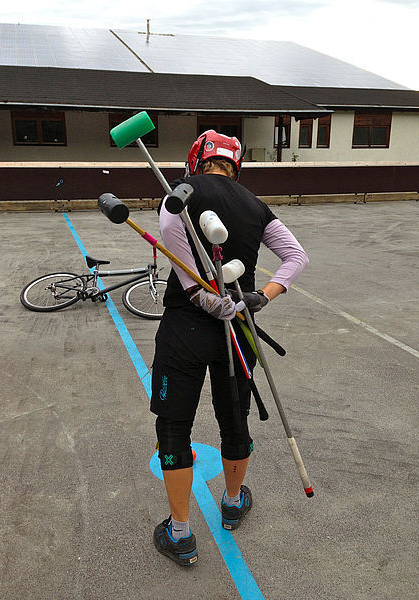 Person with red helmet carrying multiple padded poles and bicycle on ground
