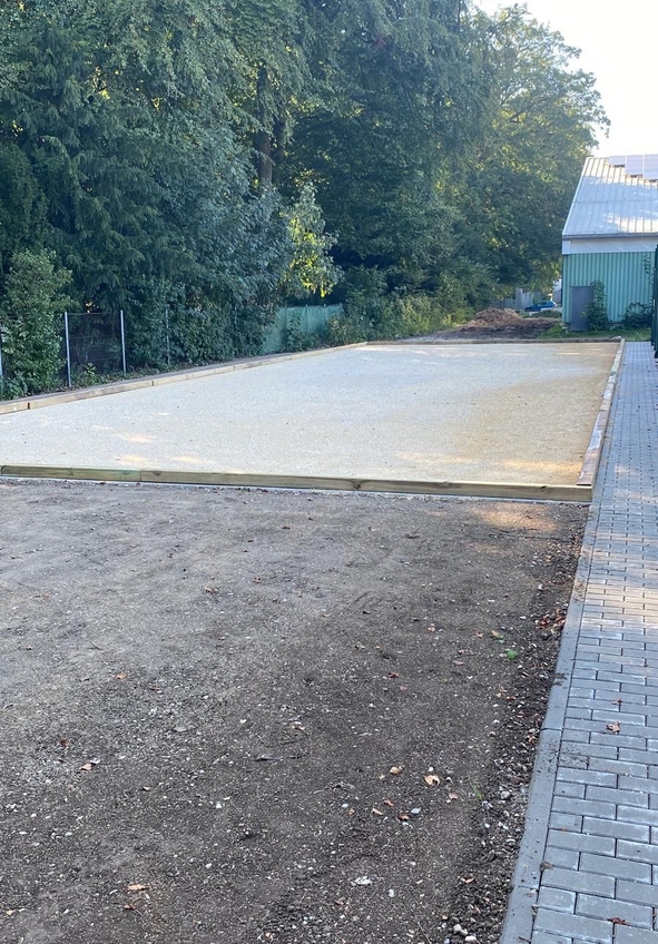 Geebnete Kiesfläche mit Holzumrandung neben gepflastertem Gehweg und Bäumen