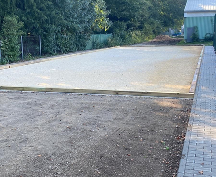Geebnete Kiesfläche mit Holzumrandung neben gepflastertem Gehweg und Bäumen