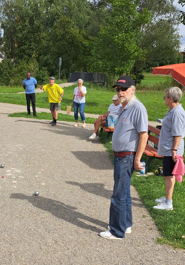 Sechs Personen spielen Boule auf Kiesfläche im Park