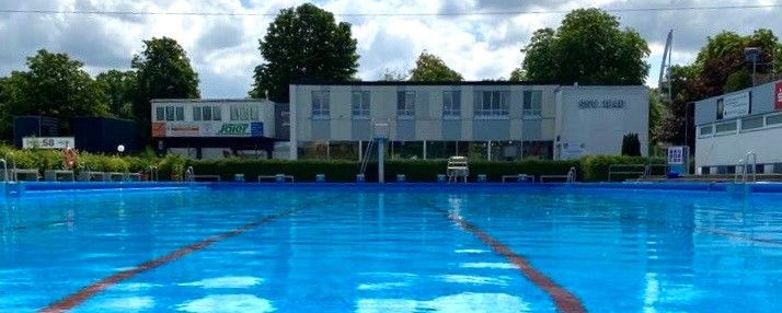 Freibadbecken mit roten Bahnmarkierungen vor Vereinsgebäude bei bewölktem Himmel