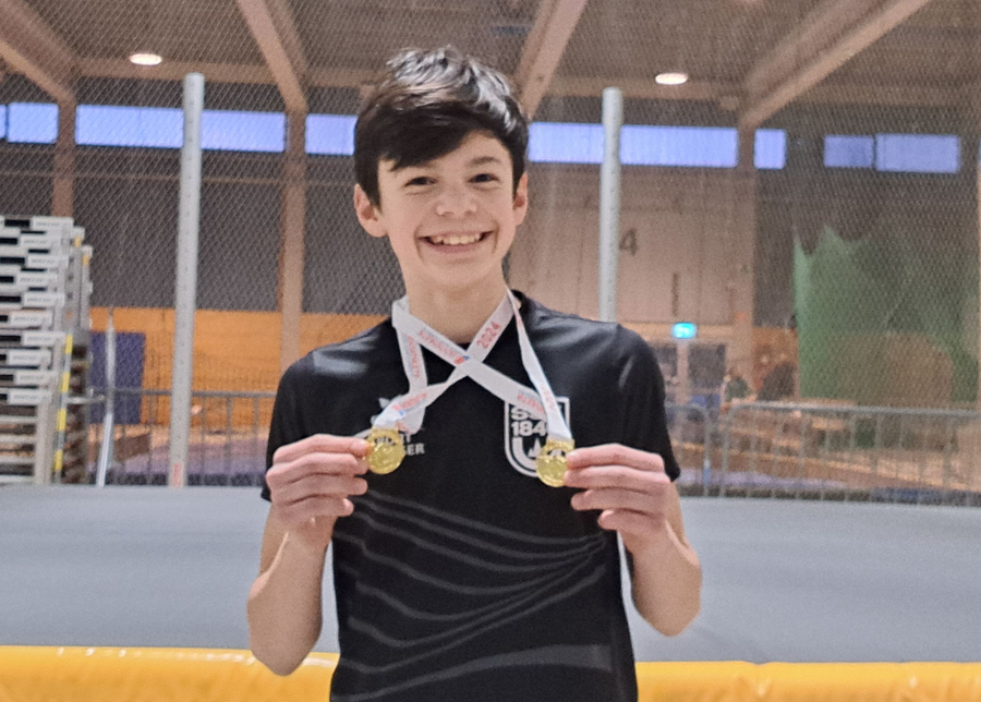 Lächelnder Junge hält zwei Goldmedaillen in Sporthalle
