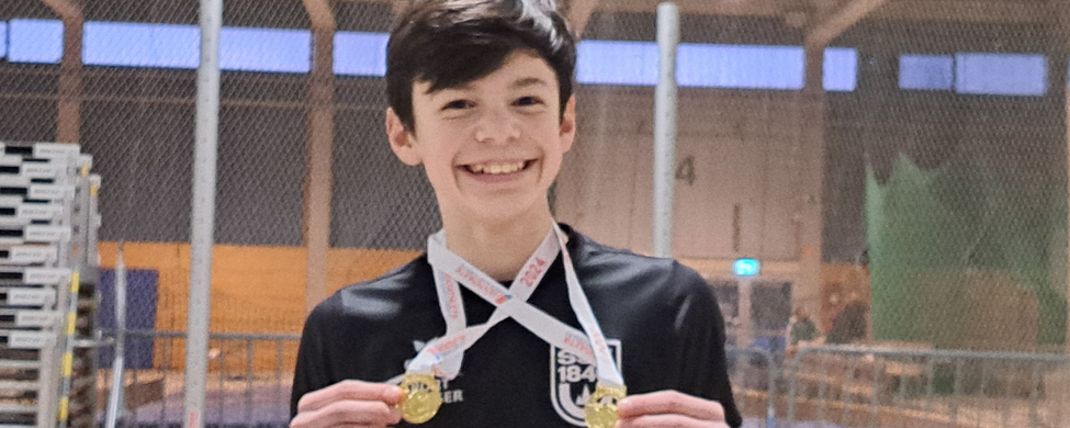 Lächelnder Junge hält zwei Goldmedaillen in Sporthalle
