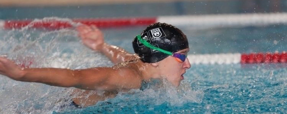Schwimmer mit schwarzer Badekappe und Schwimmbrille beim Schmetterlingsschwimmen im Wettkampfbecken
