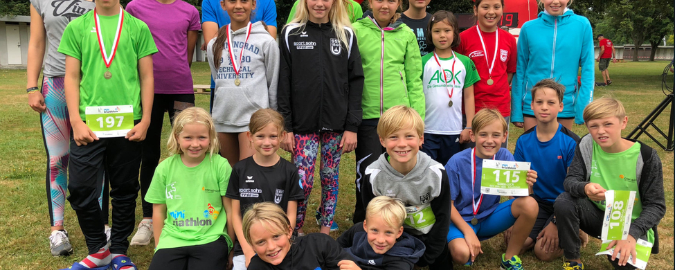 Junge Triathleten in einer Gruppe mit Medaillen und Startnummern