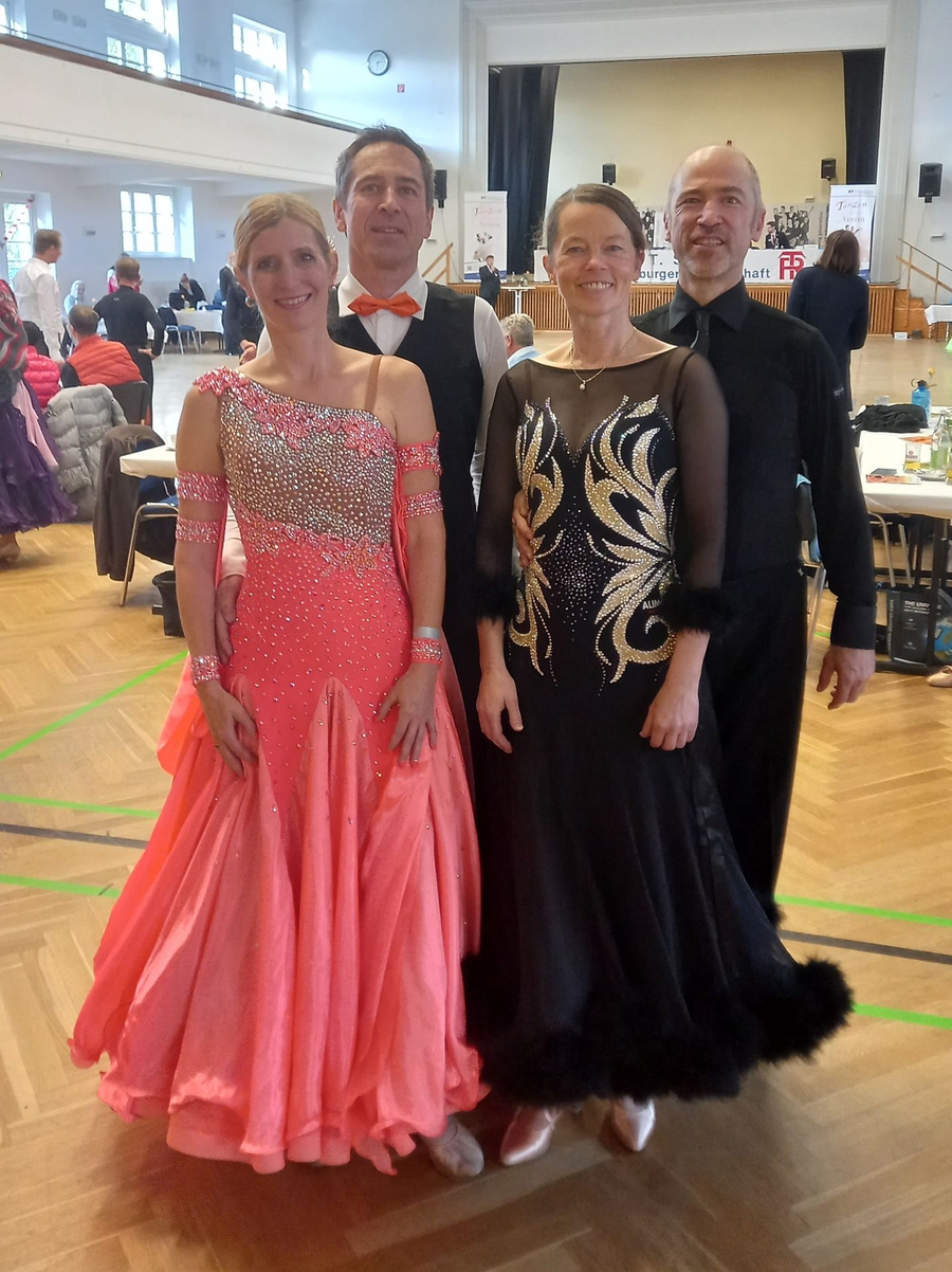 Zwei Tanzpaare in Turnierhalle, Damen in korallefarbenem und schwarzem Kleid