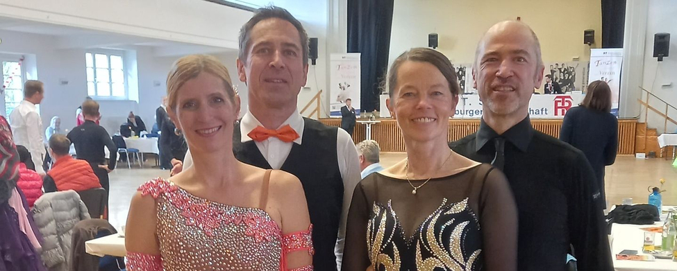 Zwei Tanzpaare in Turnierhalle, Damen in korallefarbenem und schwarzem Kleid