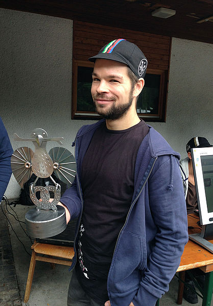 Smiling bearded man in navy hoodie holding metal trophy