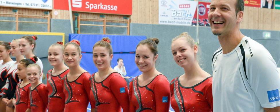 SSV Ulm Kunstturnteam in roten Trikots mit lächelndem Trainer
