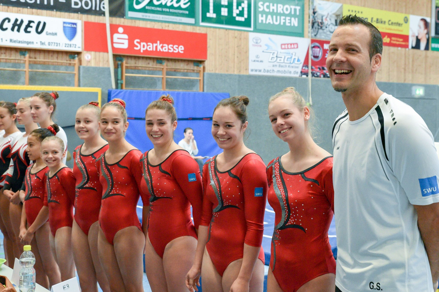 SSV Ulm Kunstturnteam in roten Trikots mit lächelndem Trainer