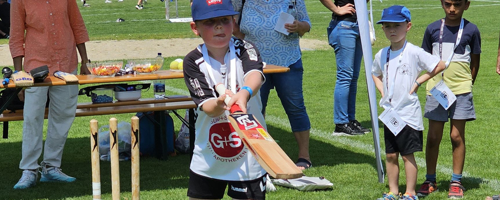 Kind schlägt mit Cricket-Schläger vor Cricket-Stand beim Schwörsporttag