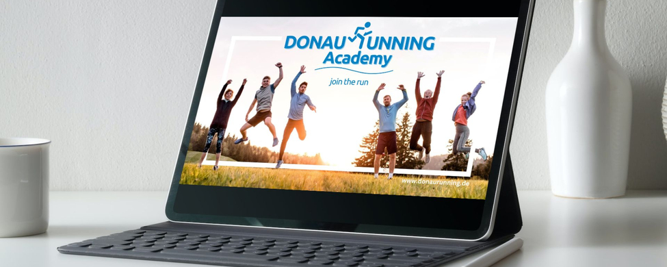 Tablet auf Schreibtisch zeigt DONAURUNNING Academy Banner mit springenden Läufern